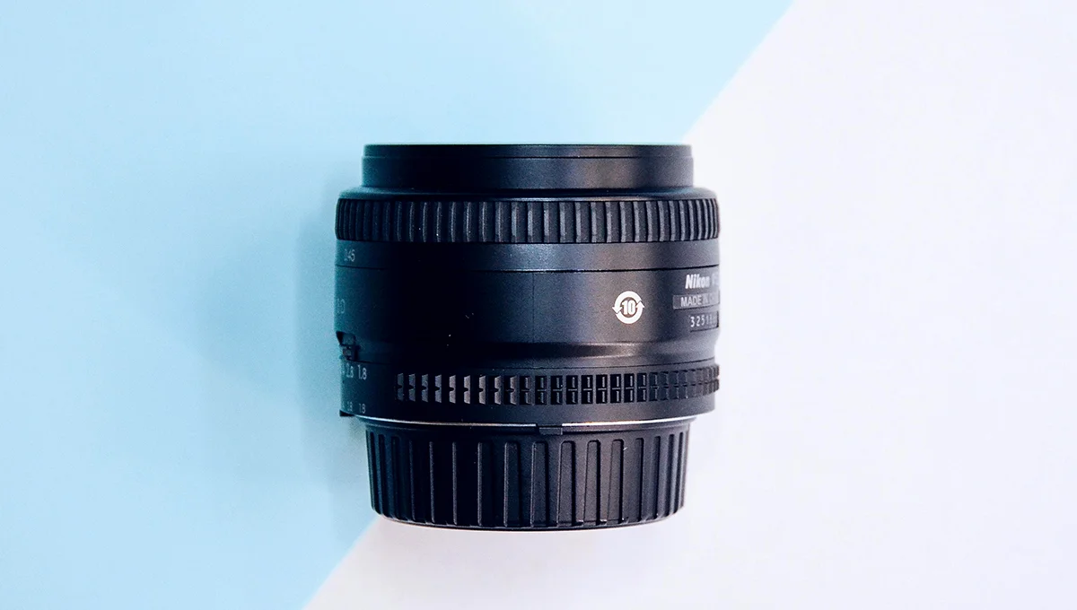 A close-up of a camera lens set against a blue and white background, highlighting its reflective surface and intricate details.