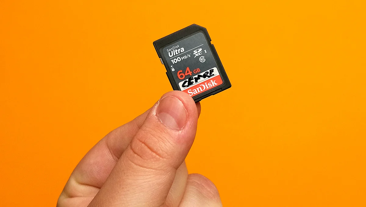 A hand holds a small memory card against a vibrant orange background, emphasizing the card's details and texture.