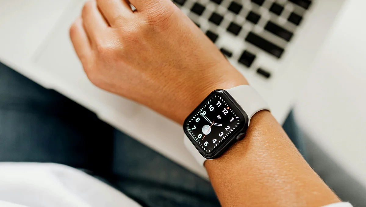 Individual in front of a laptop, with an Apple Watch visible on their wrist, focused on the screen