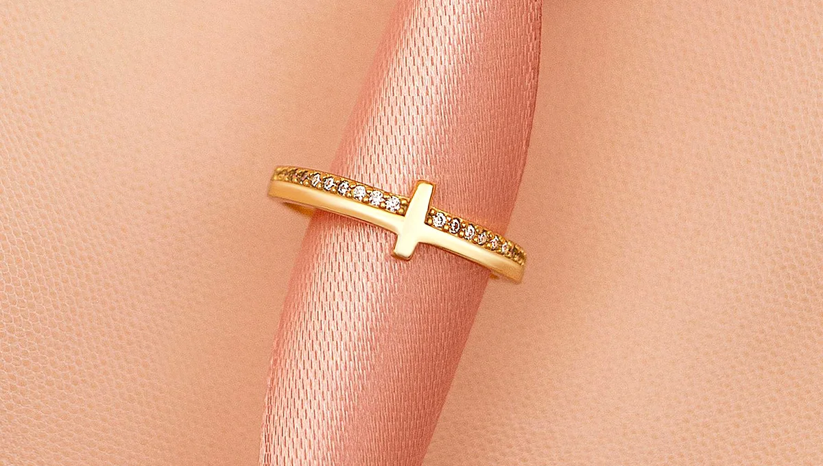A gold ring adorned with diamonds, displayed on a pink fabric background