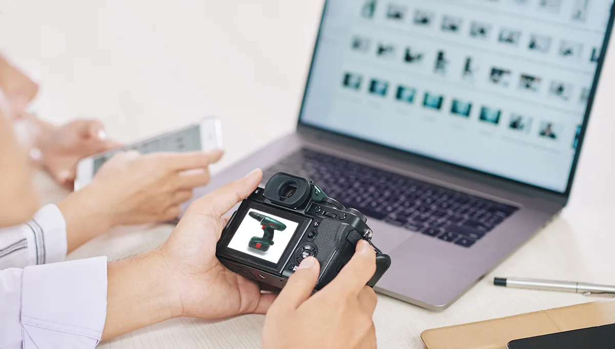 A person holding a camera while looking intently at a laptop screen, engaged in photography.