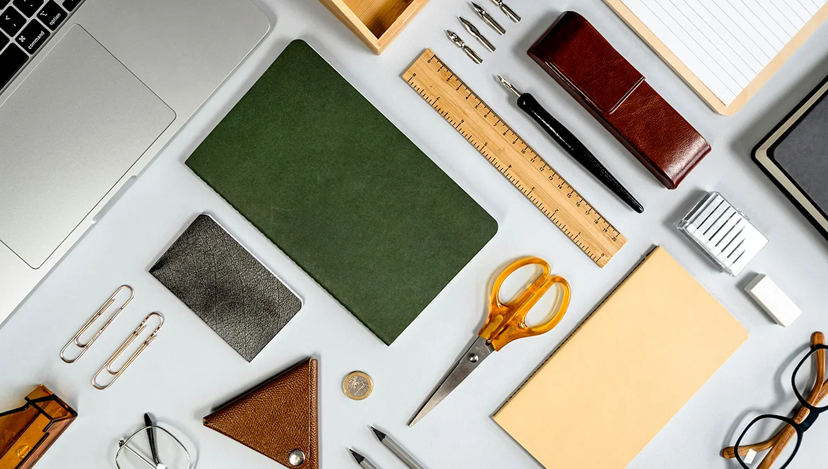 Office supplies displayed in a flat lay arrangement on a white background, featuring stationery products on a desk surface