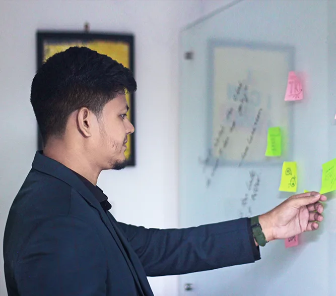 A man in a suit and coat points to a whiteboard covered with colorful sticky notes during a presentation