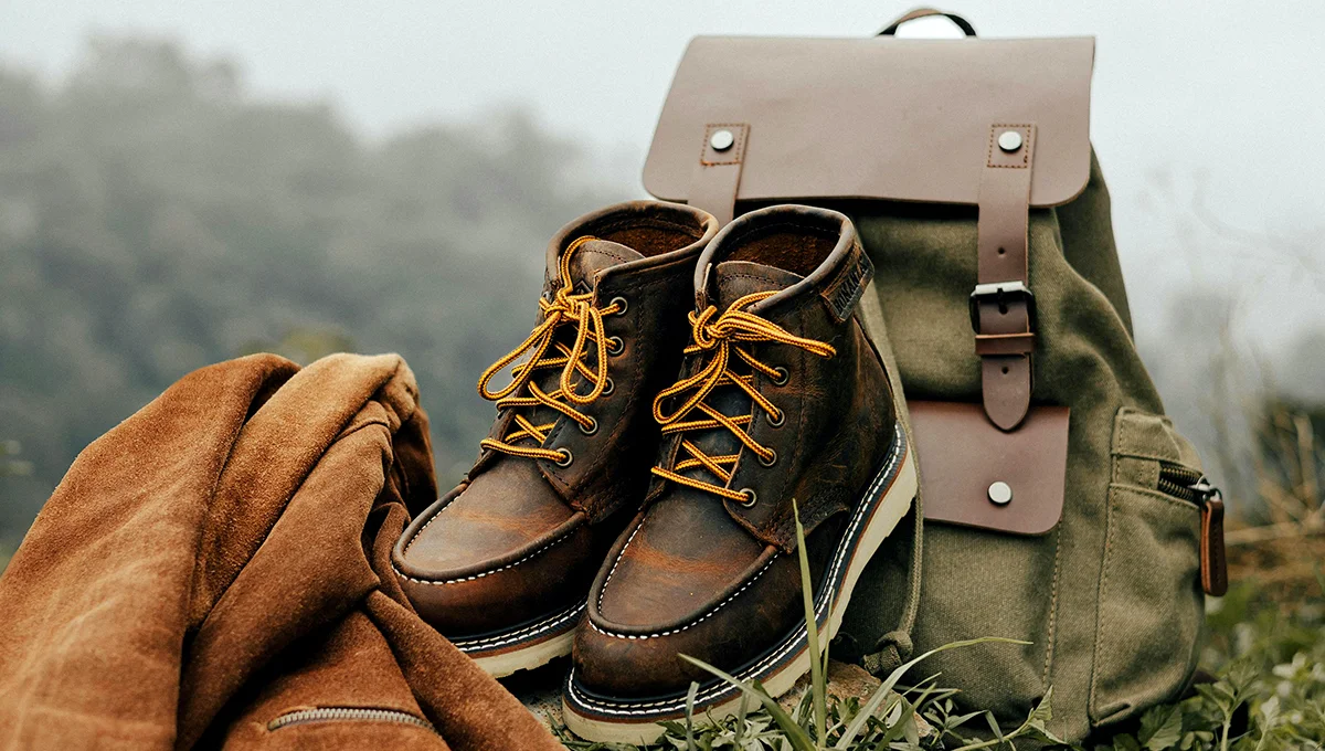 Brown boots and a backpack placed on lush green grass, suggesting an outdoor adventure or travel