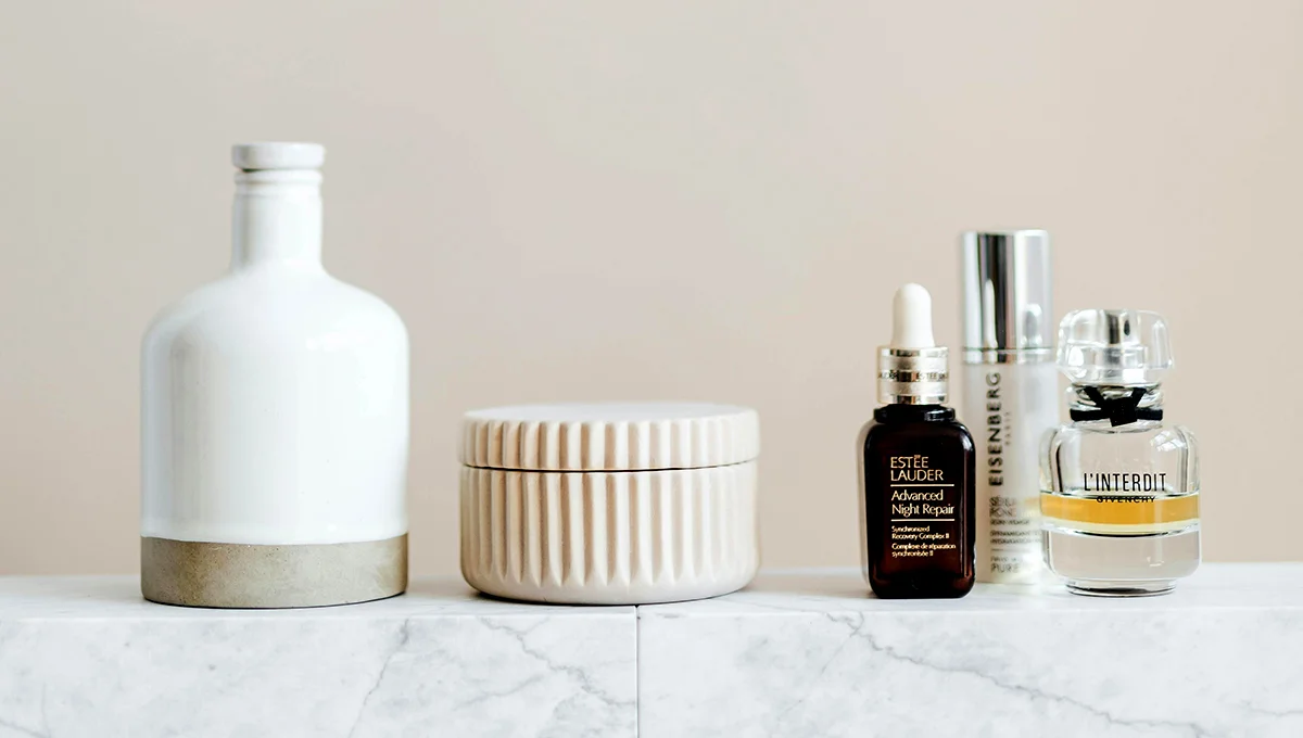 A bottle of perfume, a bottle of lotion, and another bottle of perfume arranged together on a neutral background