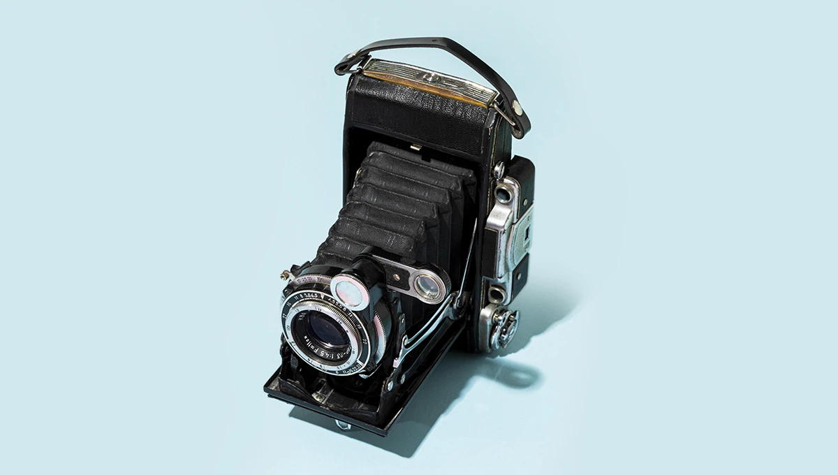 A vintage Kodak camera set against a pale blue lily background, historically utilized for product photography, highlighting its classic style