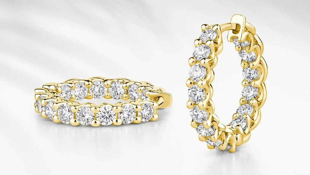 Gold hoop earrings with sparkling round diamonds set all around. One earring is upright, the other is laying flat.