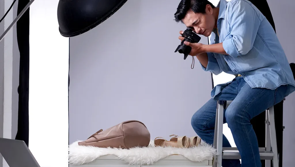 A man is photographing women's shoes and bags in a studio, highlighting techniques for product photography`